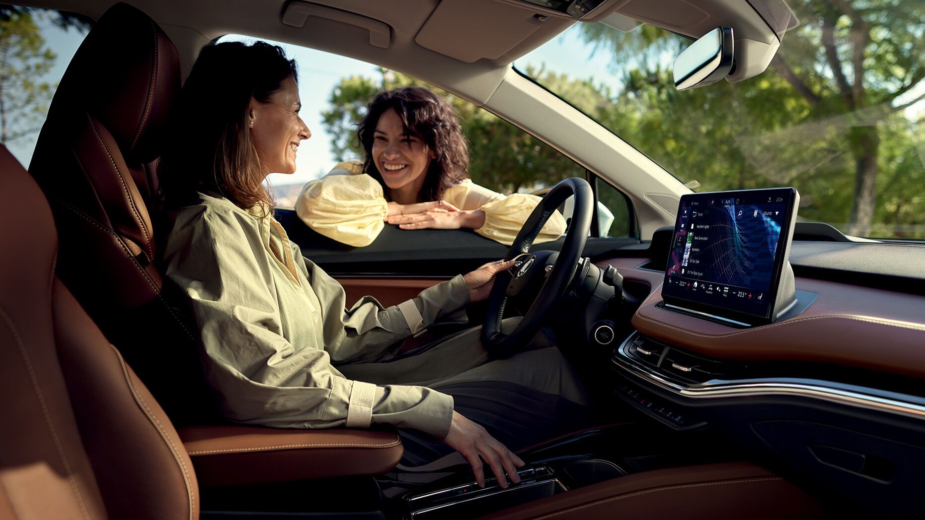 Zwei Freundinnen unterhalten sich-eine sitzt im Cockpit eines Škoda Enyaq iV