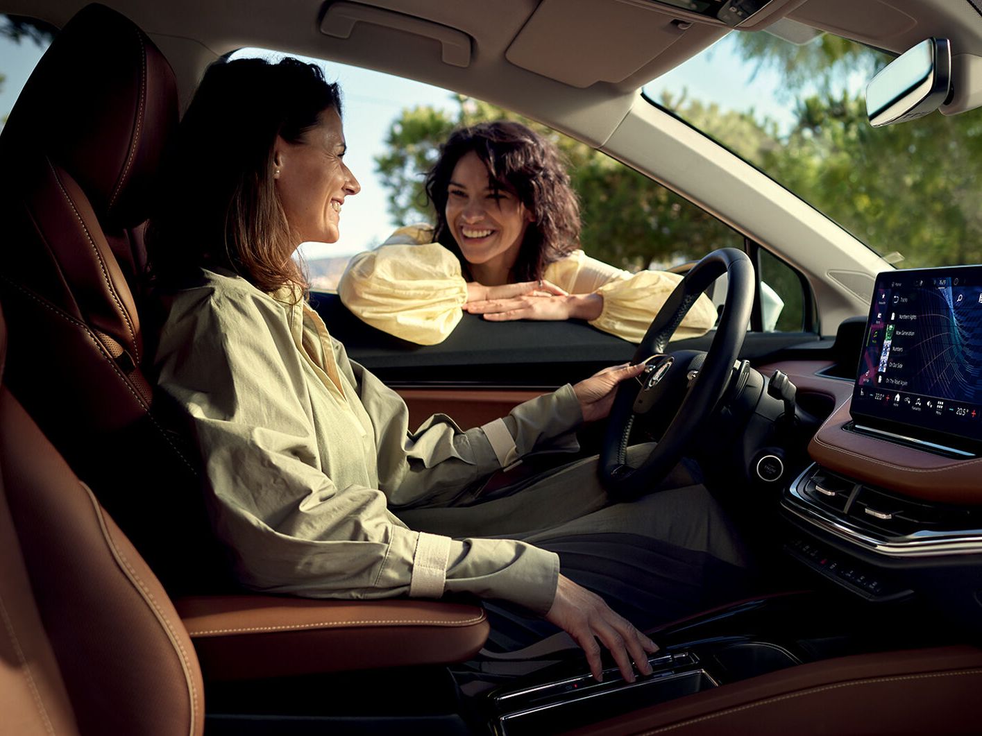 Zwei Freundinnen unterhalten sich-eine sitzt im Cockpit eines Škoda Enyaq iV