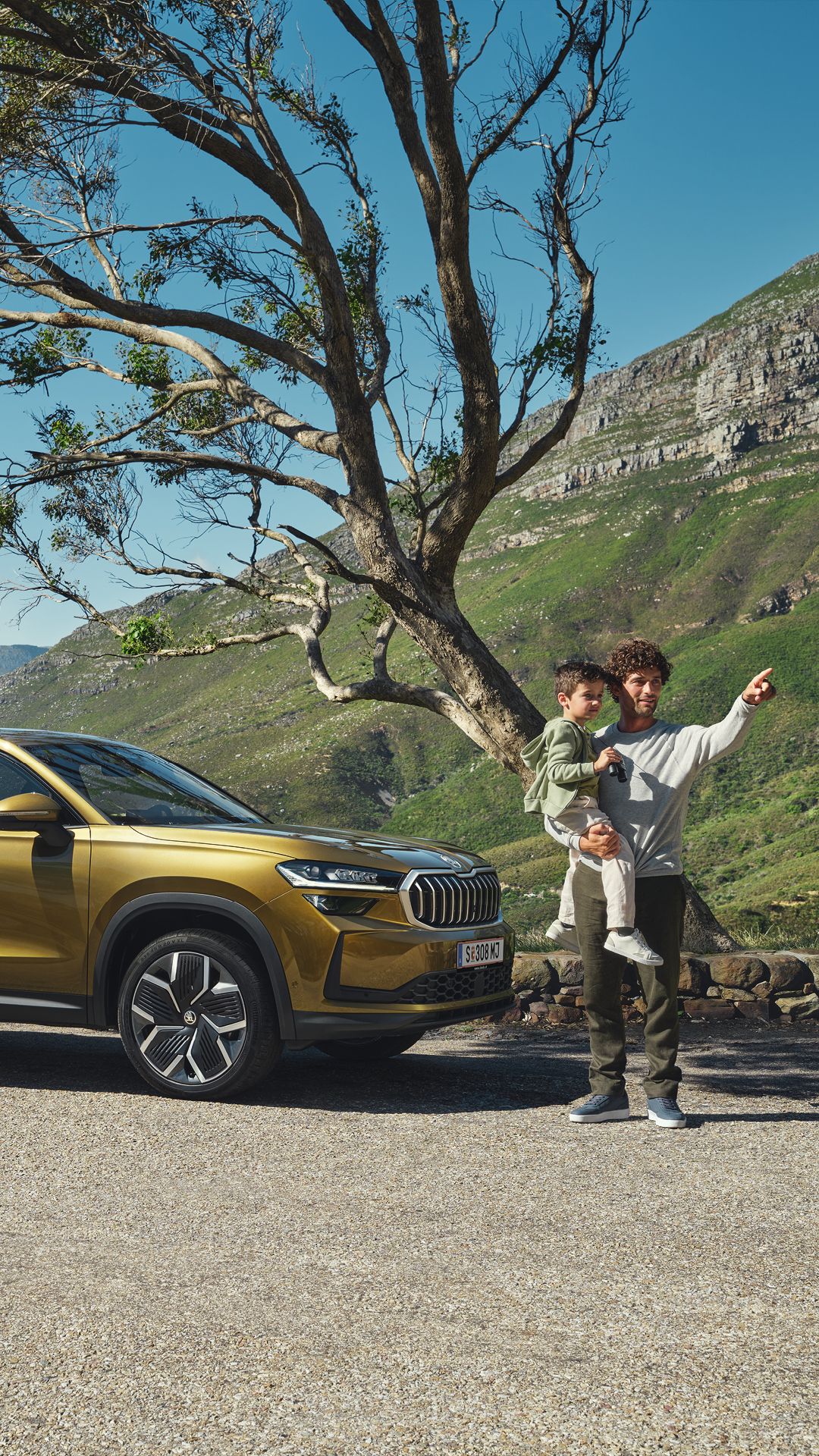 Ein Škoda Kodiaq unter einem Baum an der Meeresküste. Eine Familie steht vor dem Fahrzeug.