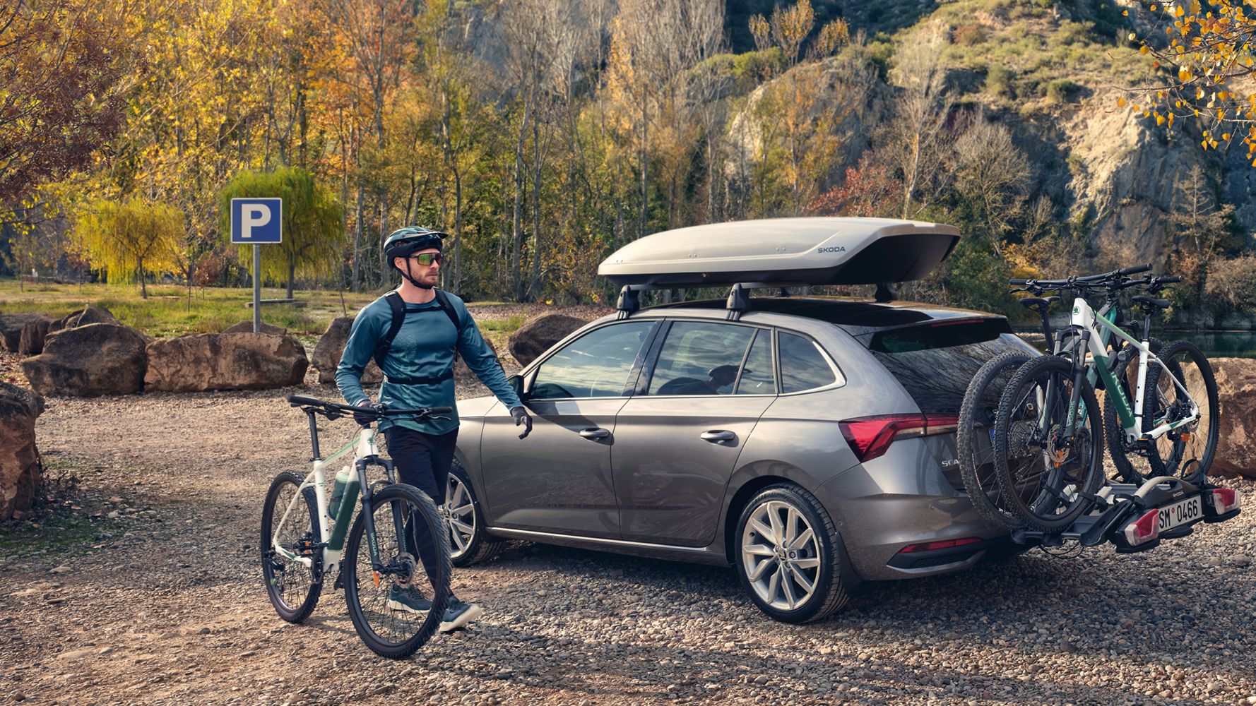 Ein Škoda Scala mit Dachbox und Fahrradheckträger, ein Mann mit seinem Fahrrad steht davor.