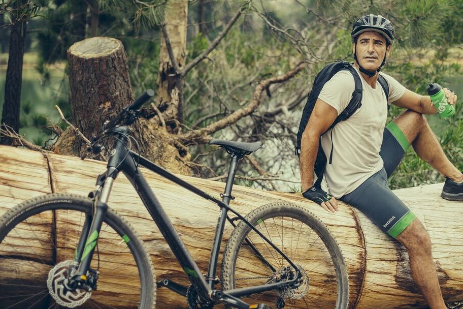 Mann sitzt auf Baumstamm, daneben ein Škoda Mountainbike