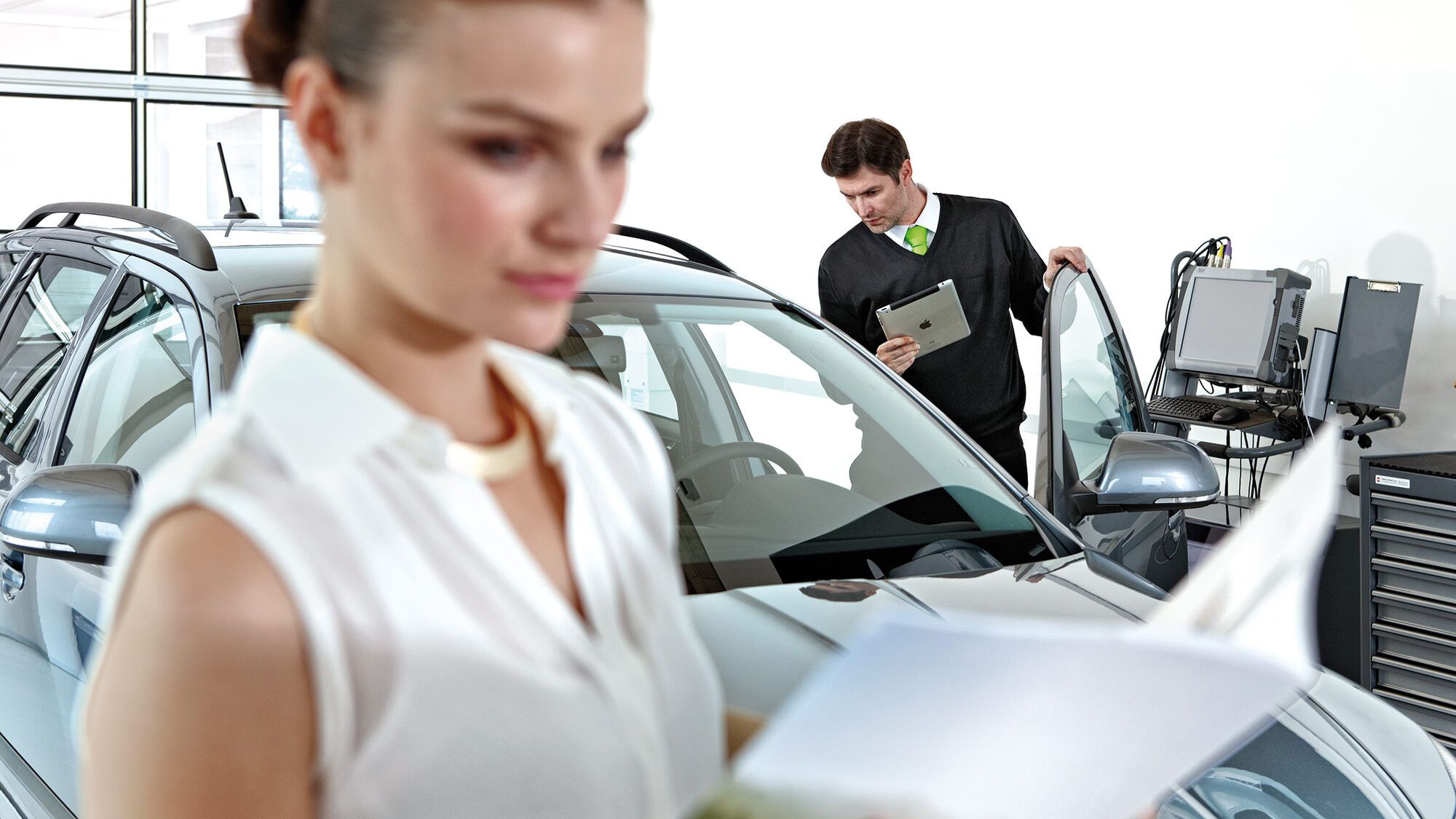 Eine Frau hält einen Prospekt in der Hand. Im Hintergrund ist ein Škoda in einer Werkstatt zu sehen.