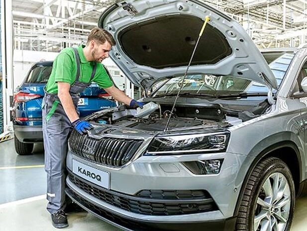 A Škoda technician pouring oil into the car engine of a silver Karoq (opened front hood)
