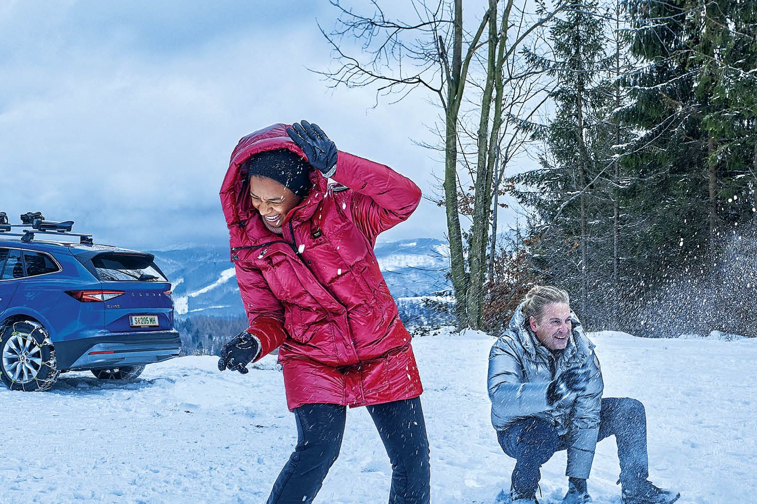 Eine Frau und zwei Männer bewerfen sich mit Schneebällen, im Hintergrund ist ein blauer Škoda zu sehen