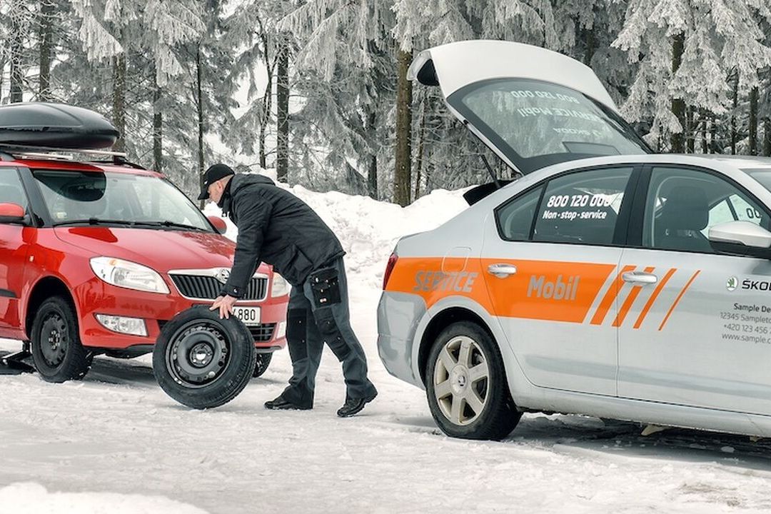 A Škoda staff changing the tyre of a red Škoda on a snowy road