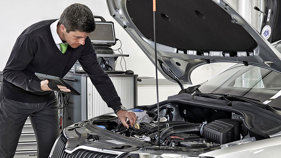 Ein Škoda Techniker mit Tablet beugt sich über die geöffnete Motorhaube von einem Škoda