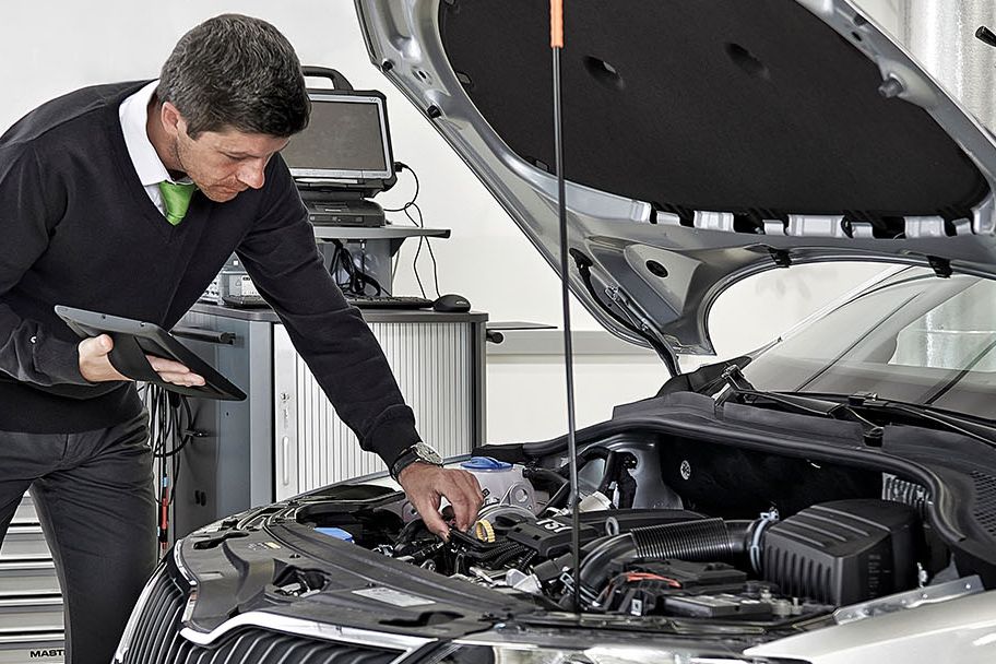 Ein Škoda Techniker mit Tablet beugt sich über die geöffnete Motorhaube von einem Škoda