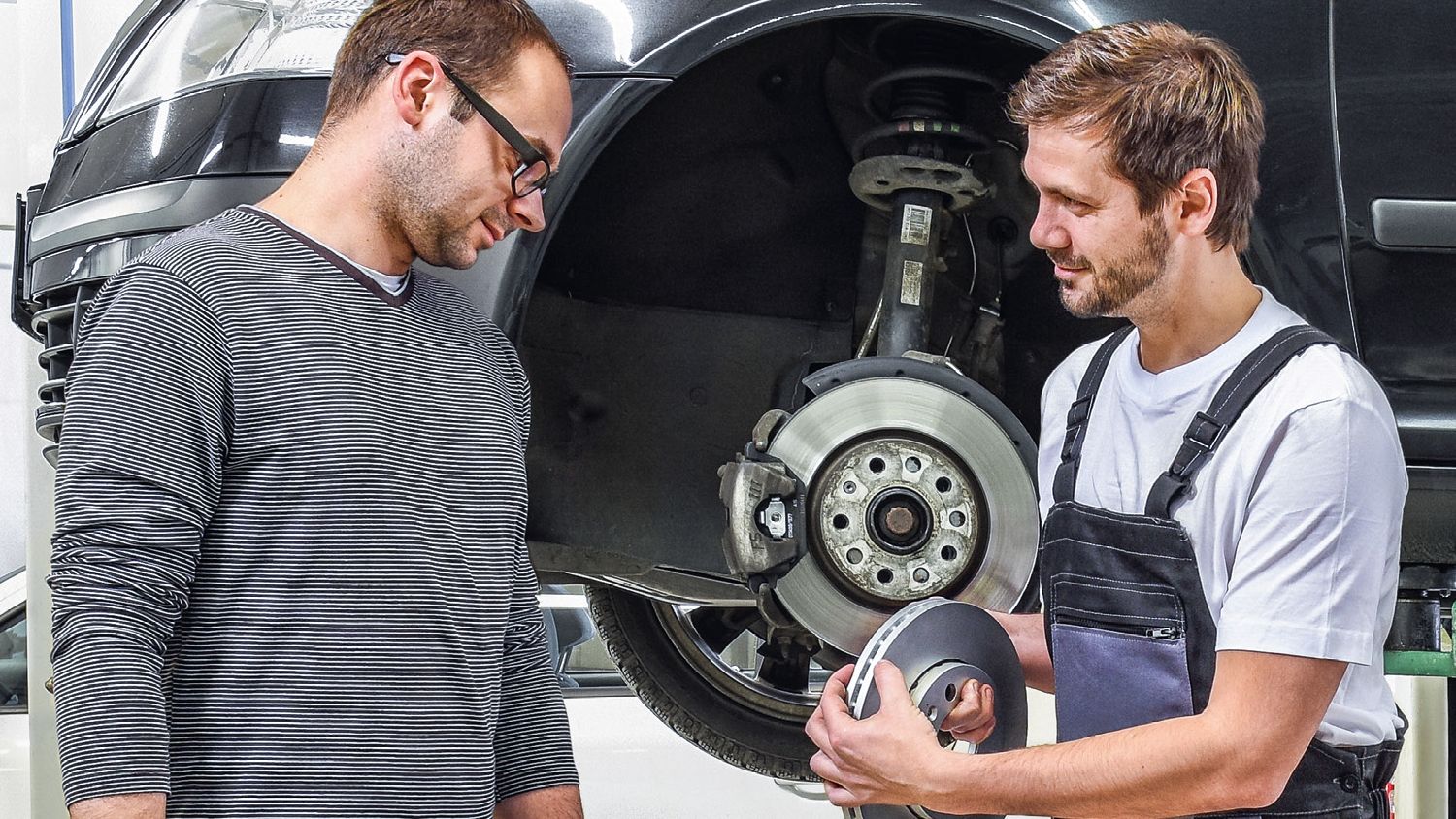 Ein Škoda Mechaniker in der Werkstatt zeigt einem Kunden die Bremsscheiben
