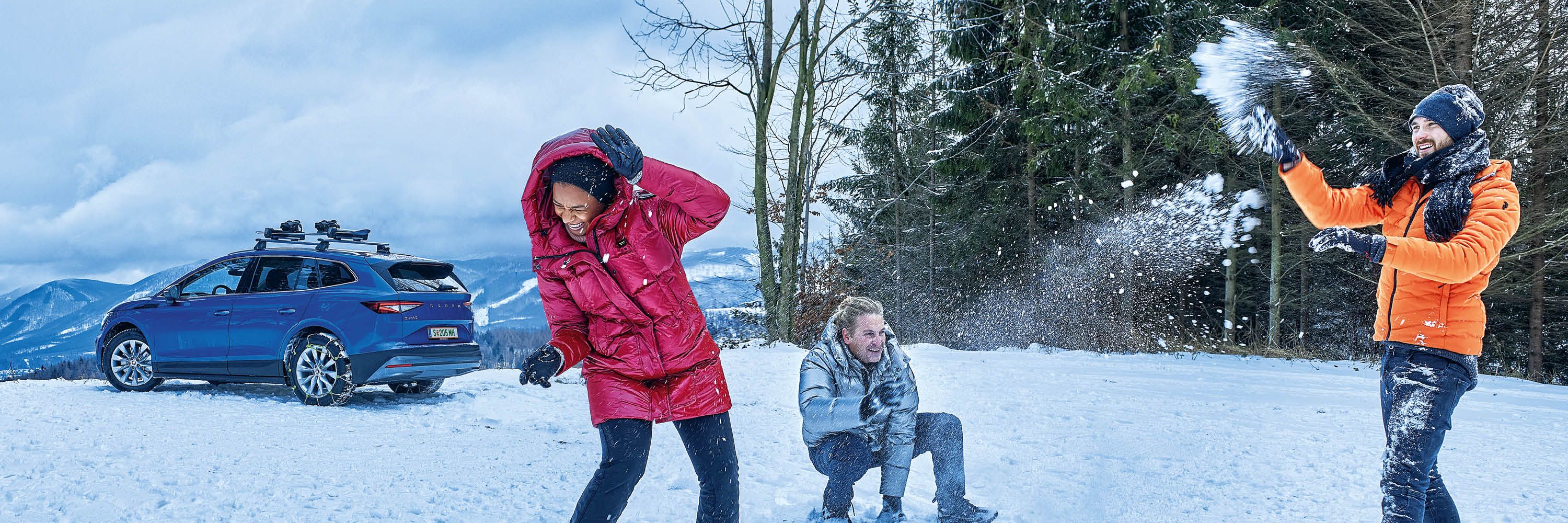 Eine Frau und zwei Männer bewerfen sich mit Schneebällen, im Hintergrund ist ein blauer Škoda zu sehen