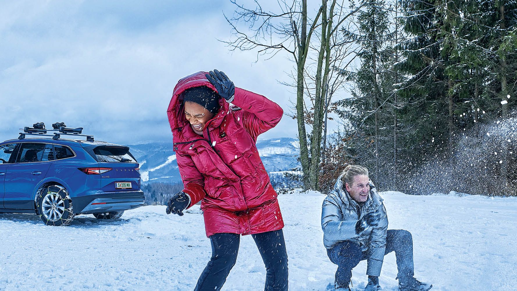 Eine Frau und zwei Männer bewerfen sich mit Schneebällen, im Hintergrund ist ein blauer Škoda zu sehen