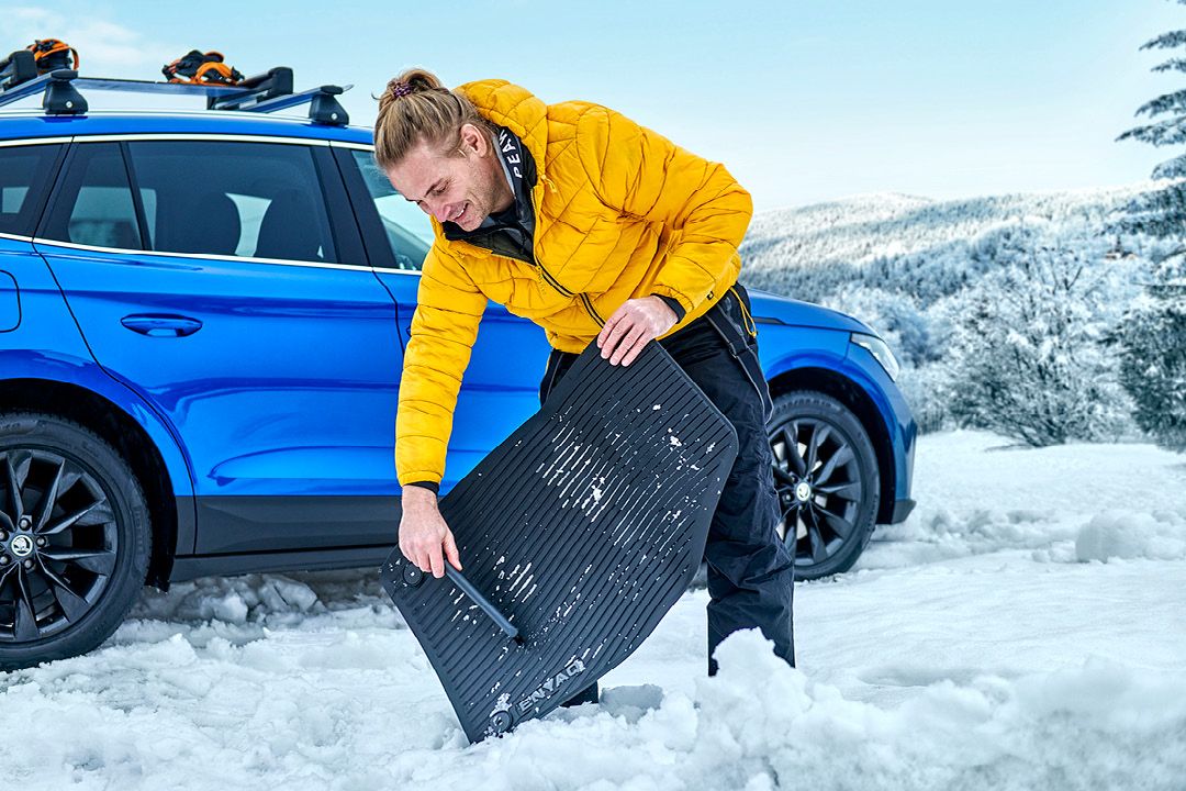 Ein Mann kehrt Schnee von einer Škoda Fußmatte