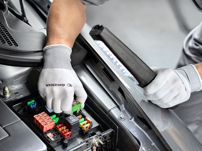 Close up view of a technician hand wearing a Škoda glove, removing a cartridge from the car engine