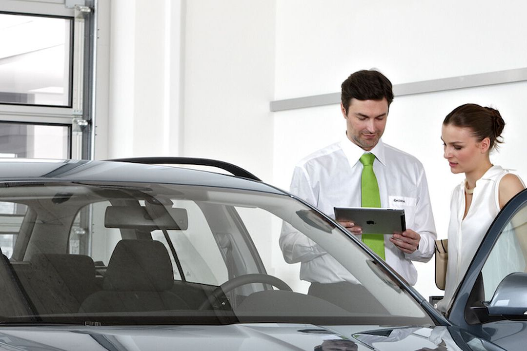 A Škoda staff showing information on a tablet to a female customer beside a grey Škoda