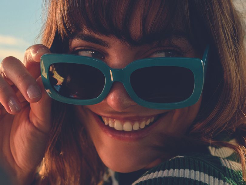 Eine Frau in einem Škoda Kamiq blickt lachend über ihre Sonnenbrille