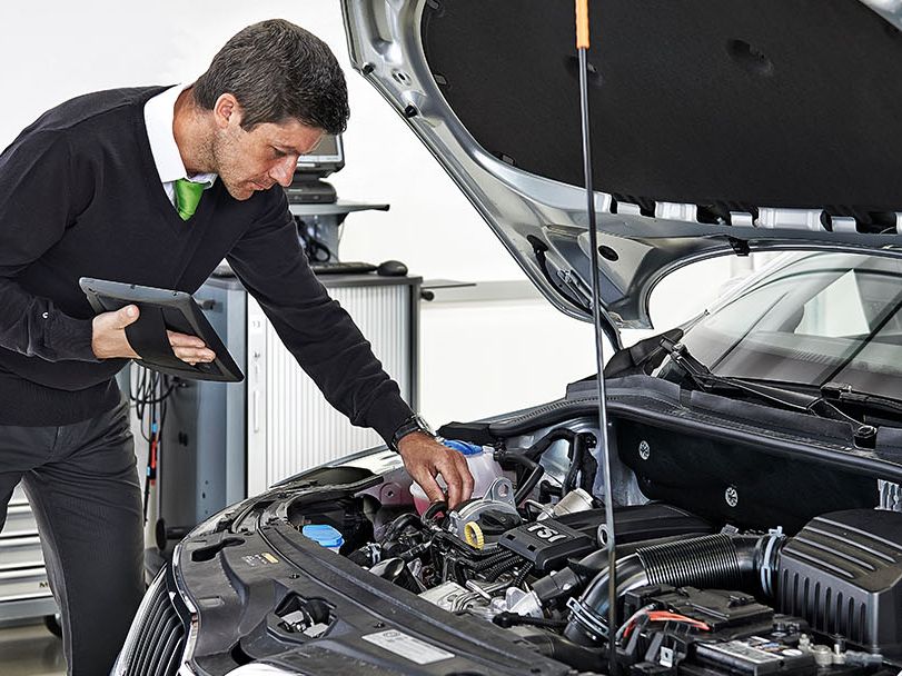 Ein Škoda Techniker mit Tablet beugt sich über den Motor eines Škoda