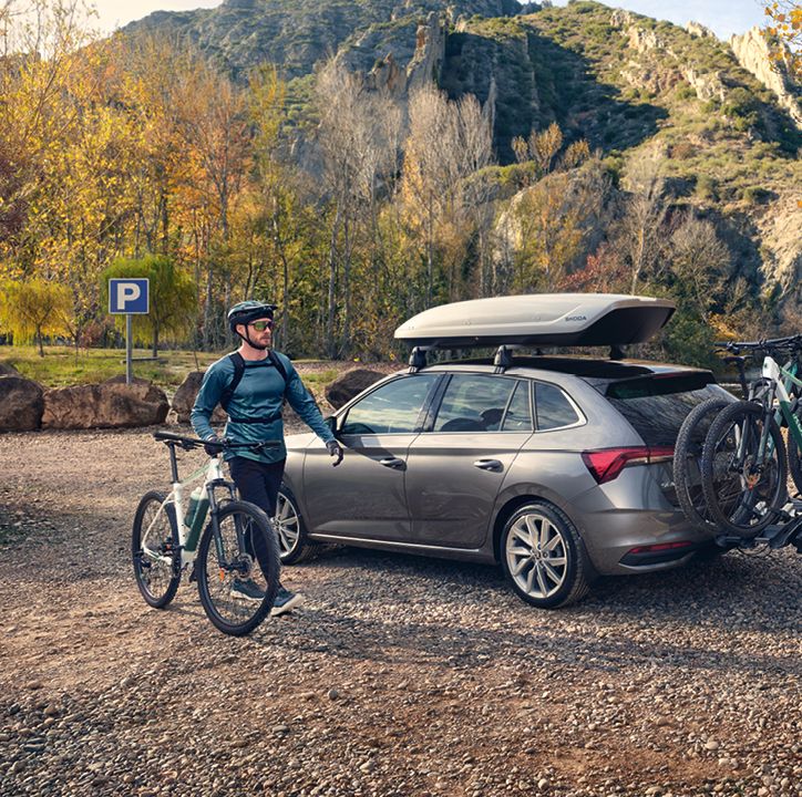 Ein Škoda Scala mit Dachbox und Fahrradheckträger, ein Mann mit seinem Fahrrad steht davor.